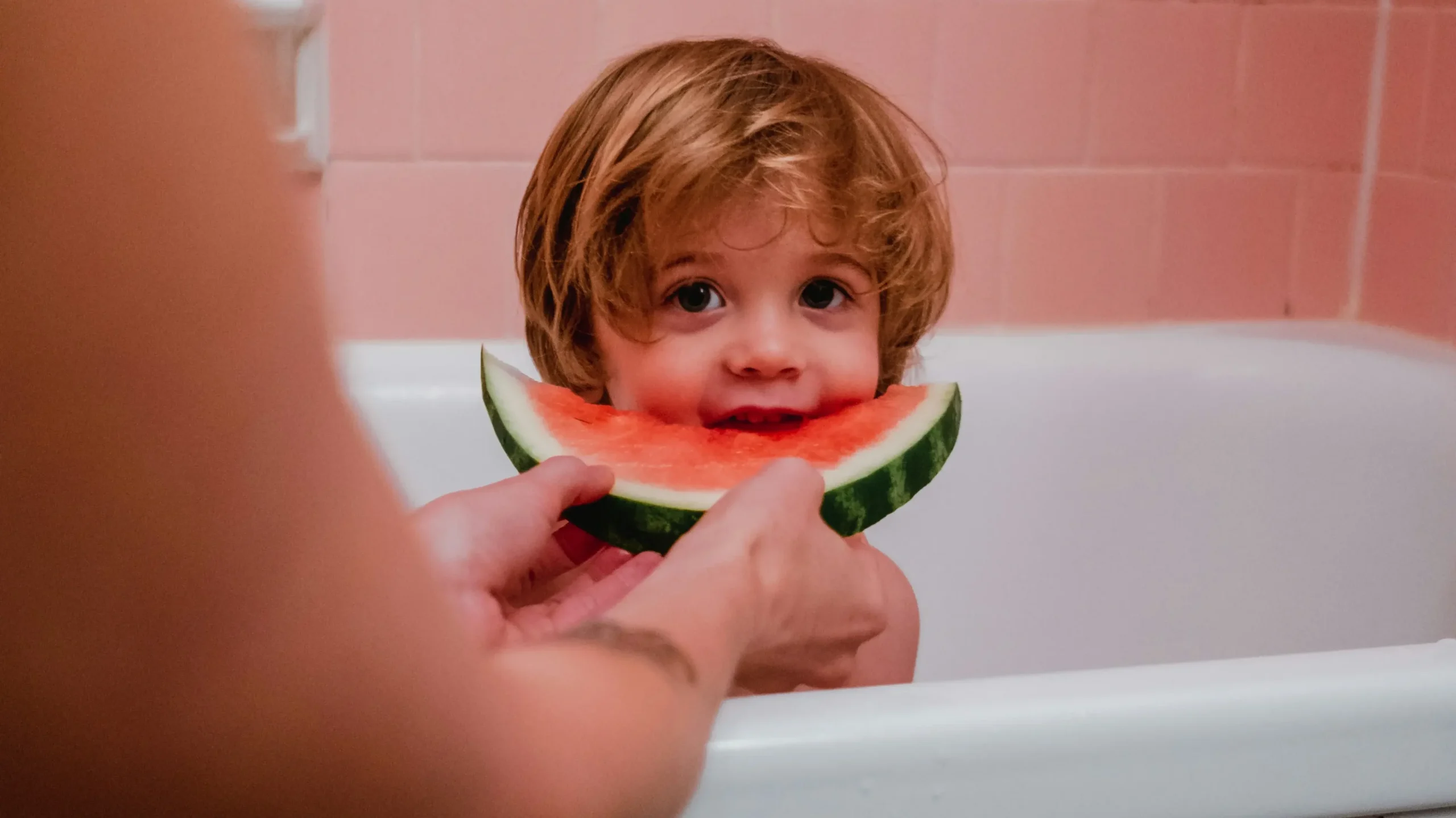 Enfant dans son bain qui croque dans une tranche de pastèque