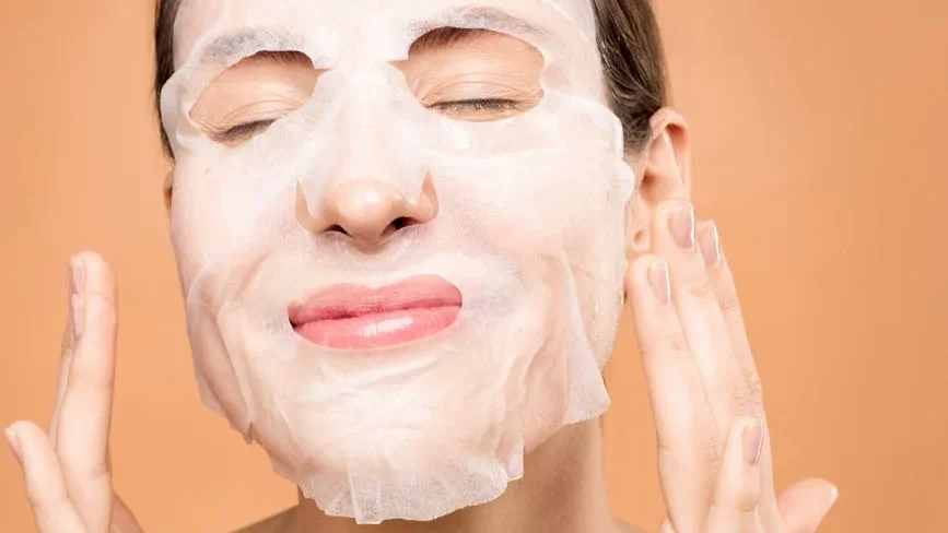 Visage souriant appliquant un masque en tissu sur fond corail